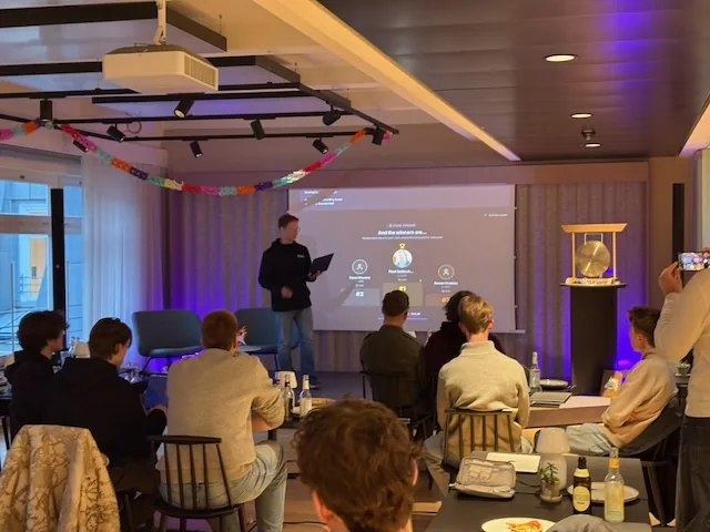 A host revealing the podium on the projector to a room of seated participants.